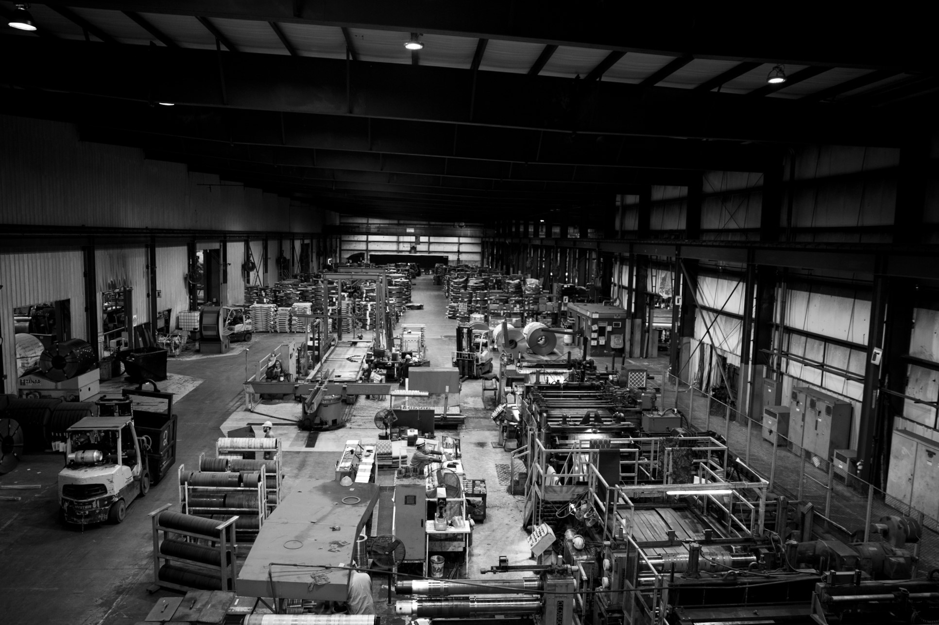Heidtman Steel Butler Facility Interior Black and white view of Heidtman Steel’s Butler facility with machinery, steel coils, and workers.