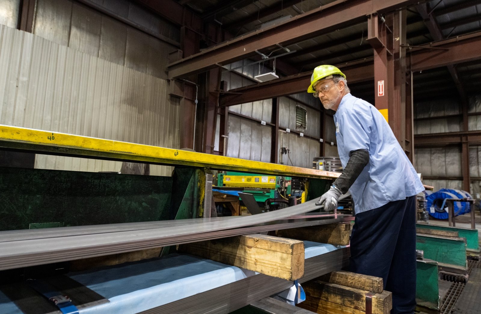Cut-To-Length Process with Steel Sheets Worker in a safety helmet handling steel sheets during the cut-to-length process in an industrial facility.