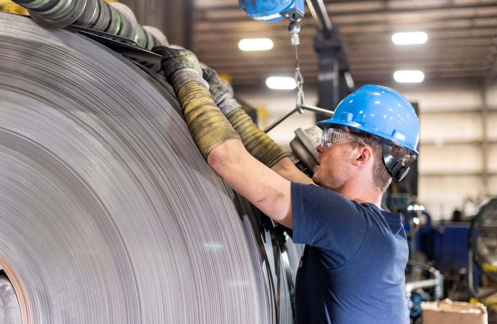 Finished Steel Coil After Edging Worker in safety gear inspecting the final result of the steel edging process on a large steel coil.