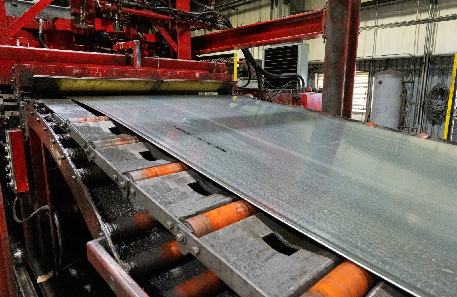 Steel Leveling Process on Industrial Line Steel sheet undergoing the leveling process on a red industrial production line, ensuring flatness and quality.