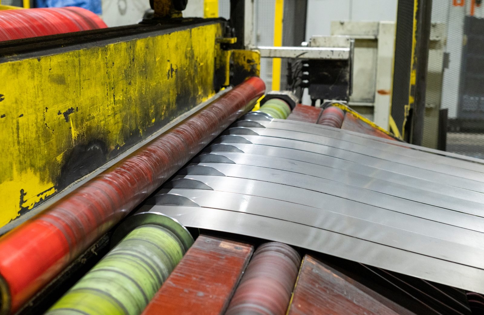 Steel Slitting Process with Precision Blades Close-up of steel strips being precisely slit into narrower widths on an industrial slitting machine.